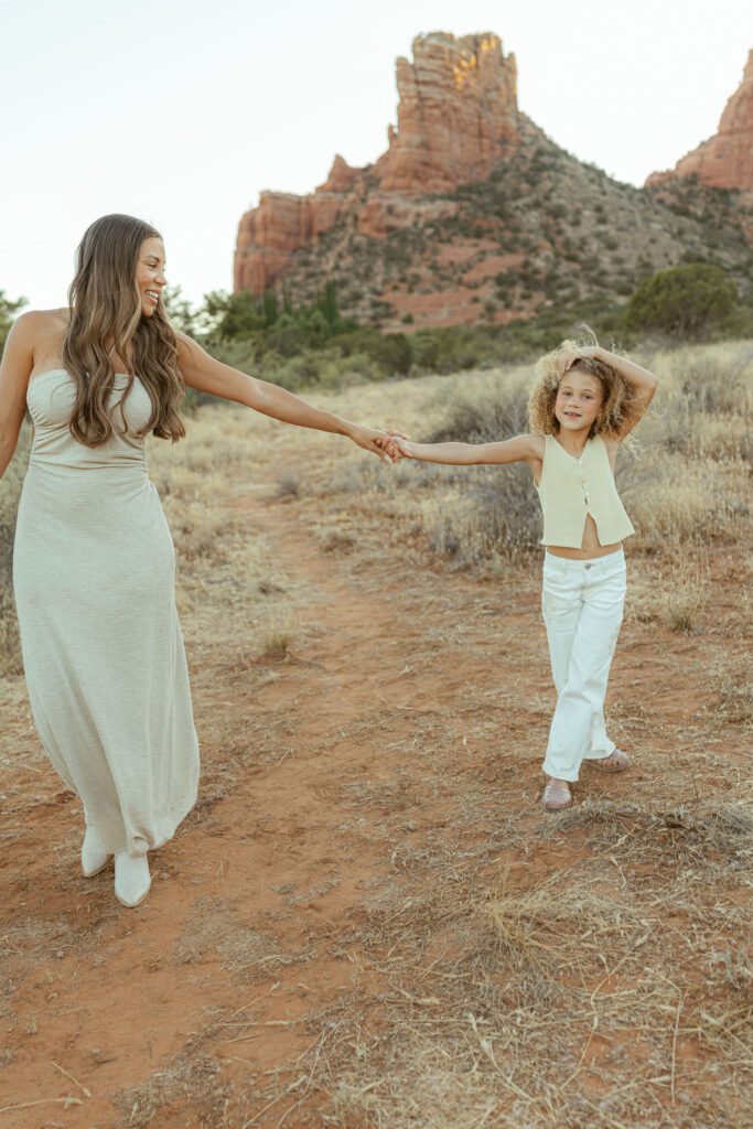 Mother and daughter holding hands during a joyful Sedona family photography session with Cathedral Rock rising behind them at sunset.
