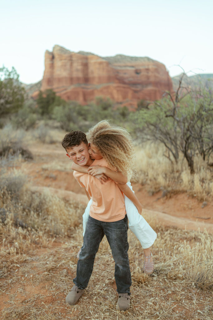 Brother giving his little sister a piggyback ride during a candid family photography session in Sedona, Arizona.