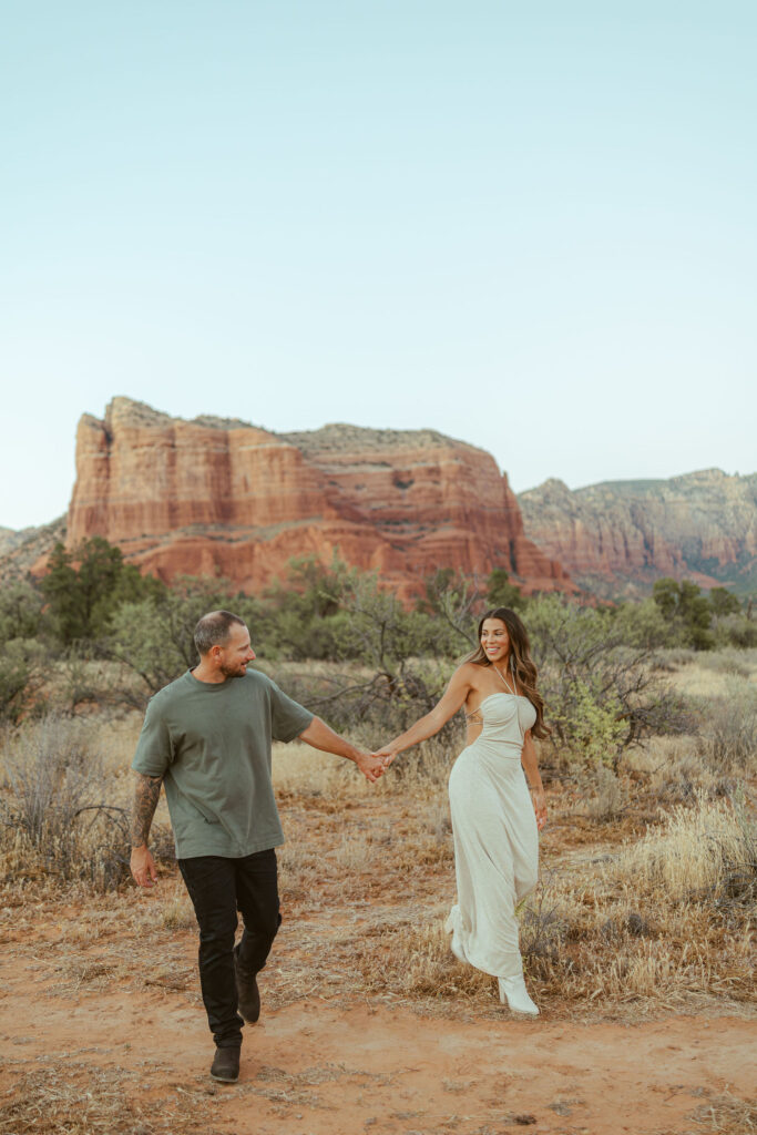Parents holding hands while walking together during a romantic couples portrait in Sedona with dramatic red rock views behind them.