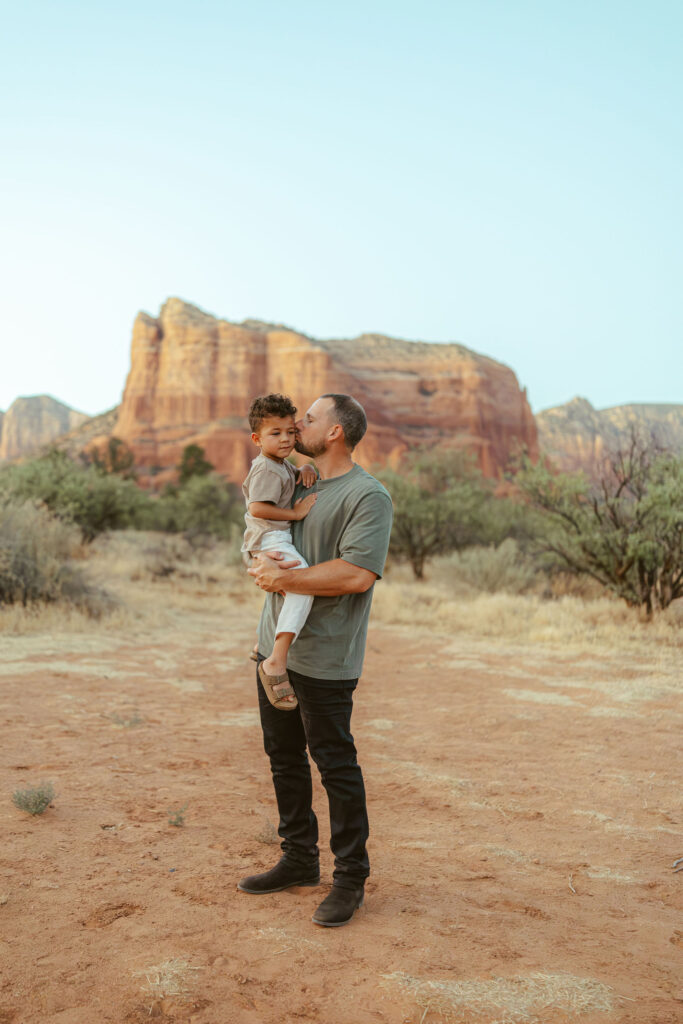 Father holding his young son during a family vacation photography session in Sedona with Arizona's stunning red rock landscape in the background.