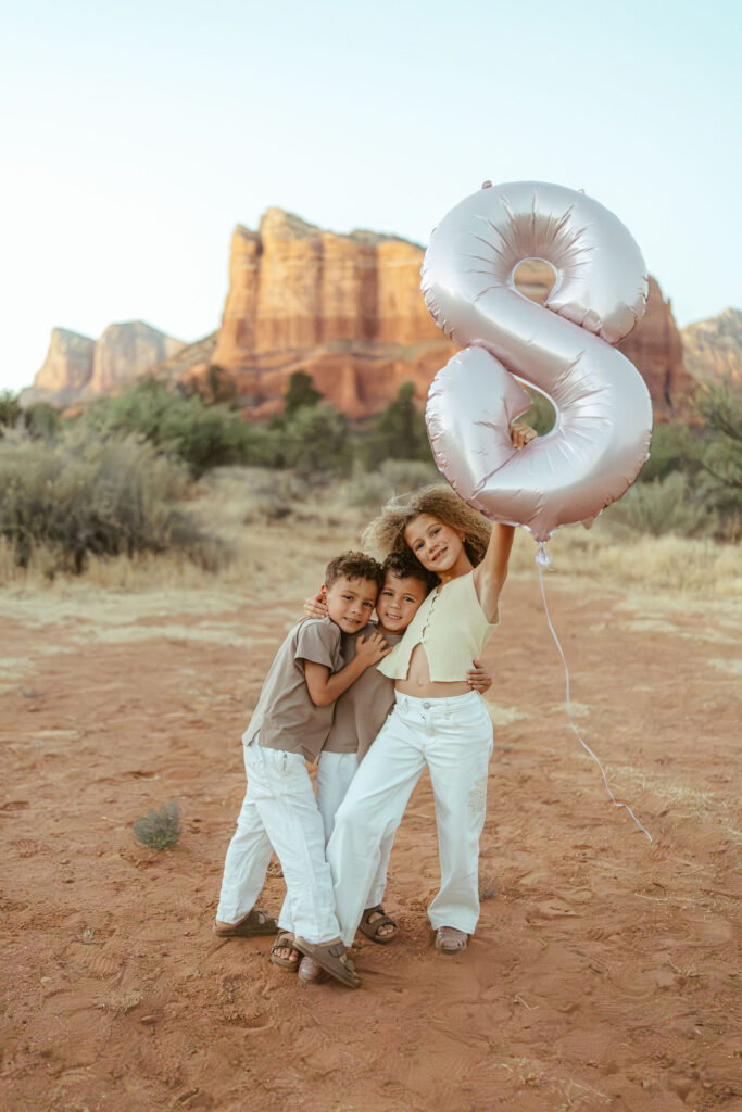 Children hugging their mother while celebrating with a silver birthday balloon during a family vacation photo session in Sedona.