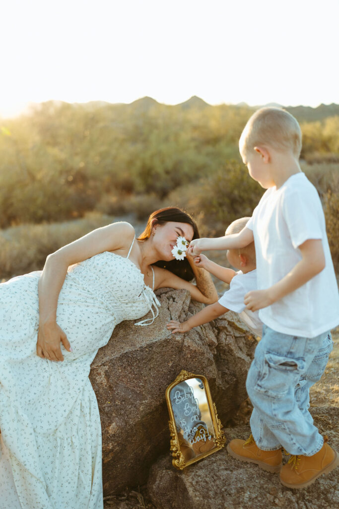 Big brother smelling a flower beside pregnancy announcement sign in the Arizona desert