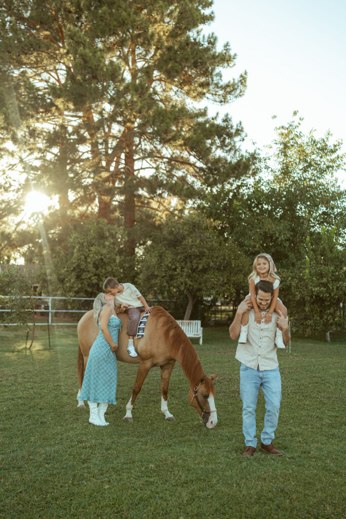 Pregnancy announcement with older siblings featuring a growing family sharing a candid moment beside their horse at sunset in Gilbert.