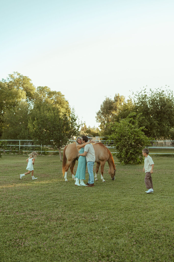Lifestyle pregnancy photography showing an expecting family hugging beside their horse during a sunset maternity session at Floyd Family Farms.