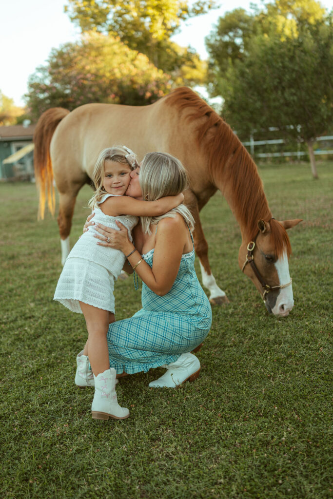 Mother and daughter maternity photos capturing a sweet hug beside the family's horse during a golden hour pregnancy announcement session.