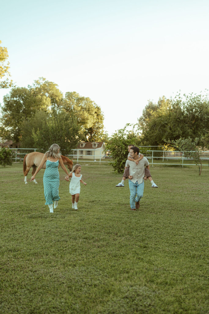Outdoor family photography in Gilbert documenting an expecting family walking through the pasture with their children during a horse-themed maternity session.