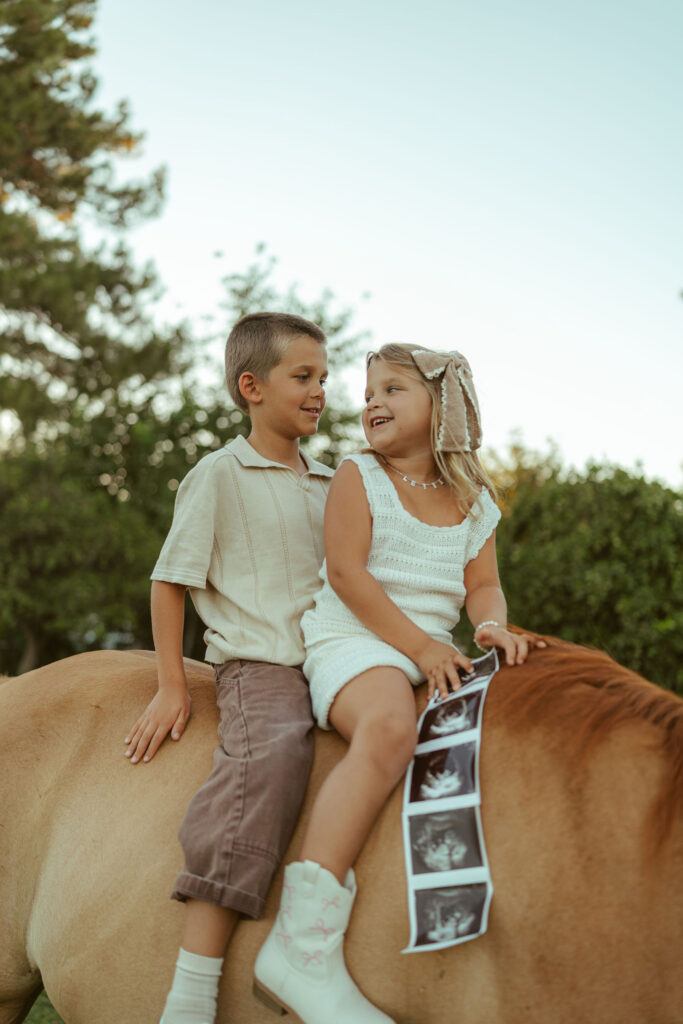 Outdoor family photography capturing an expecting family gathered beneath their horse during a relaxed farm maternity session in Gilbert.