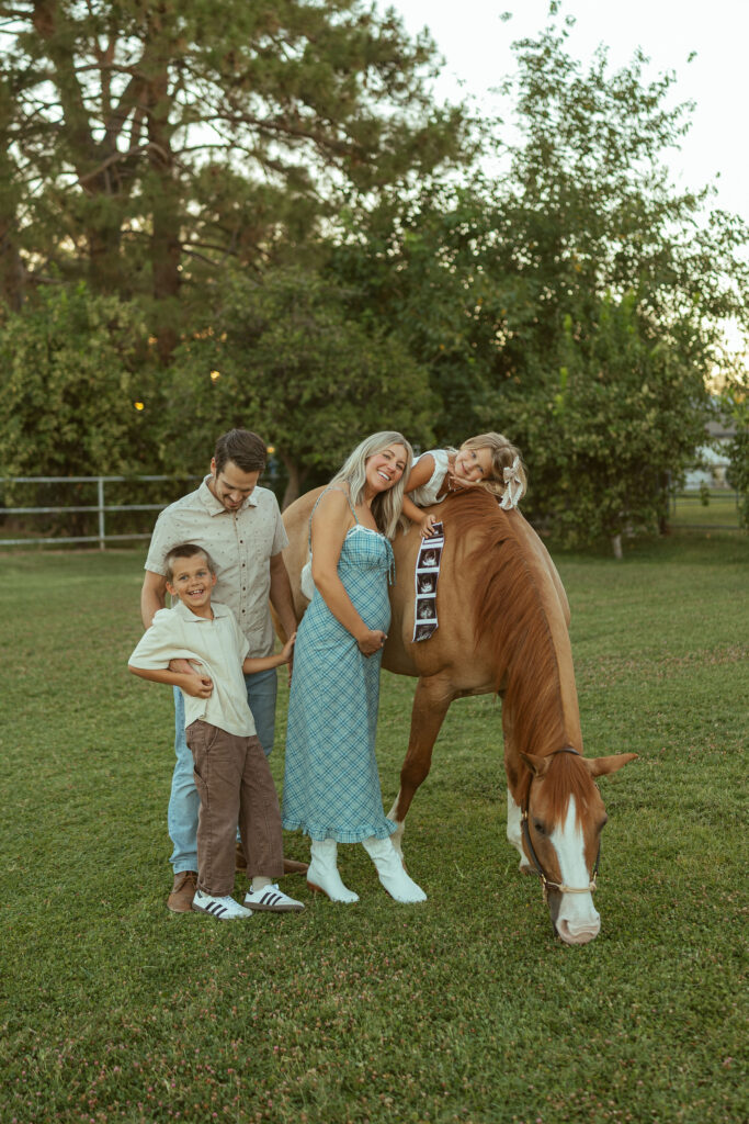 Outdoor pregnancy announcement capturing parents walking beside their horse while children run through the pasture at Floyd Family Farms.