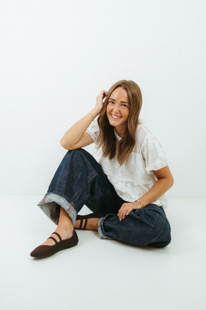 Young woman sitting on the studio floor in jeans and a white blouse during an 18th birthday photography session in Queen Creek.