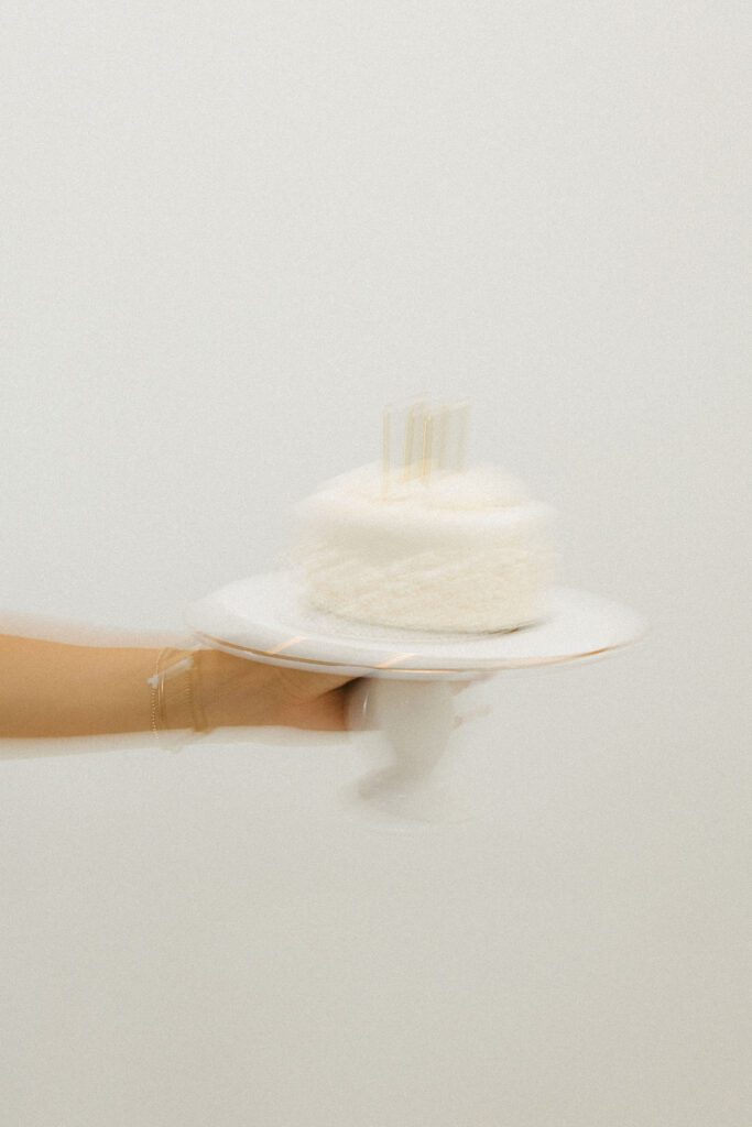 White birthday cake with lit candles photographed on a cake stand during an 18th birthday studio portrait session.