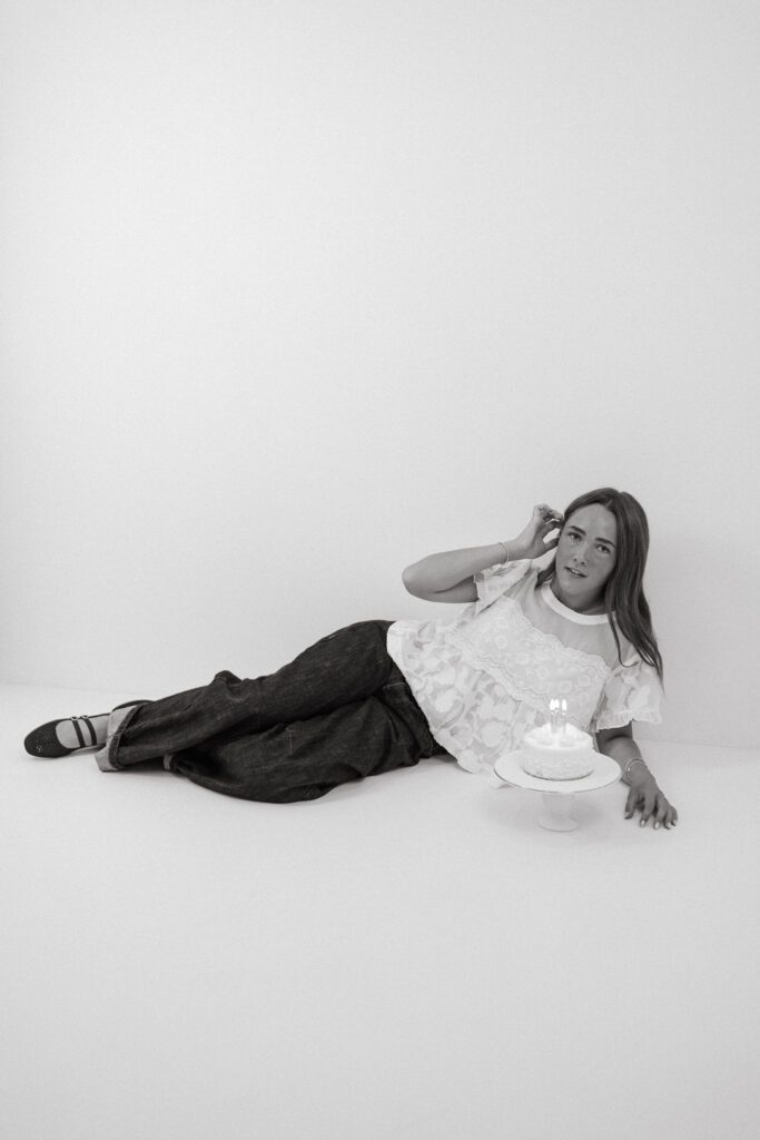 Black and white portrait of a young woman sitting beside her birthday cake in a Queen Creek photography studio.
