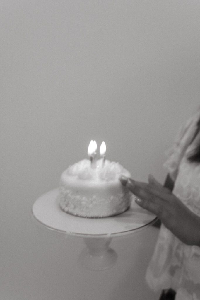 Black and white photograph of a young woman with her birthday cake and lit candles in a studio.