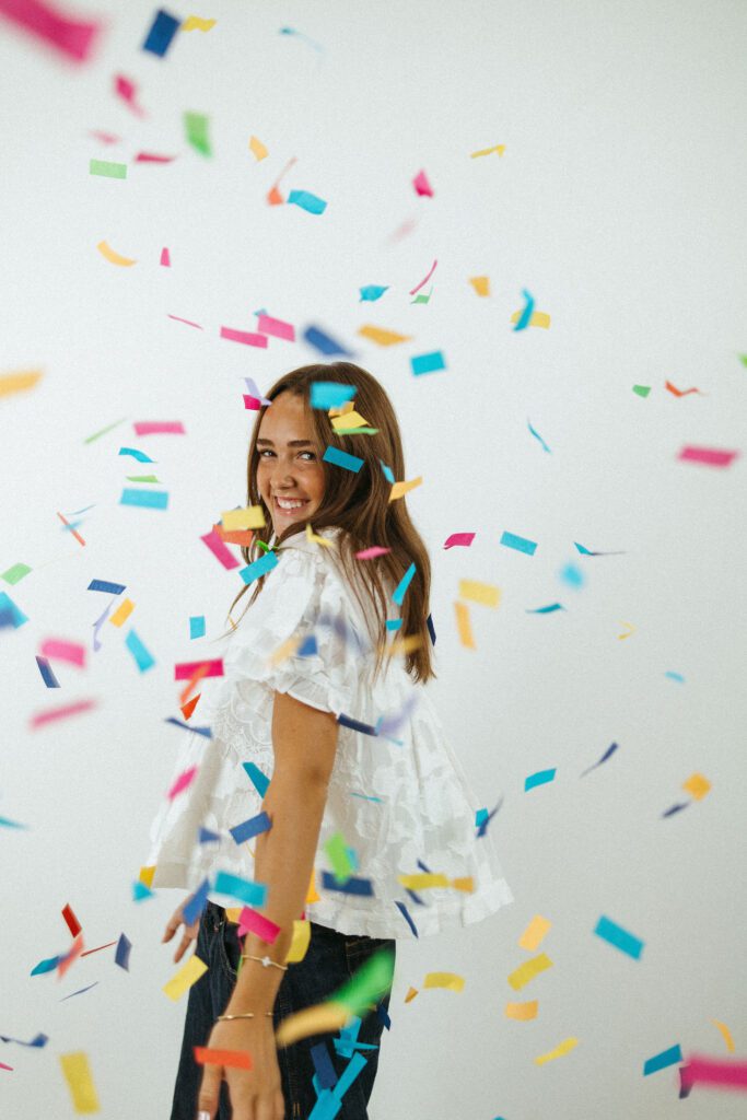 Creative 18th birthday portrait of a young woman surrounded by colorful falling confetti in a photography studio.