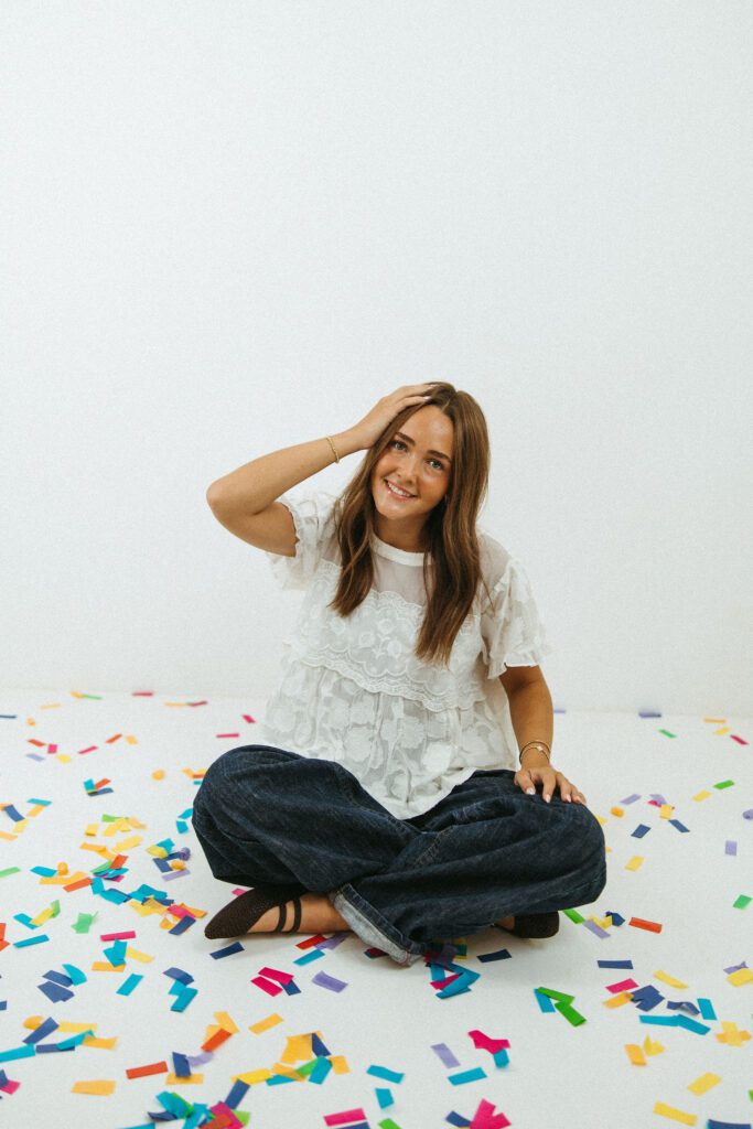 Young woman sitting on the studio floor surrounded by colorful confetti during her 18th birthday photo session in Queen Creek.