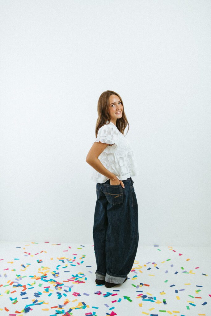 Full-body portrait of a young woman standing among colorful confetti during an 18th birthday photography session in Queen Creek.