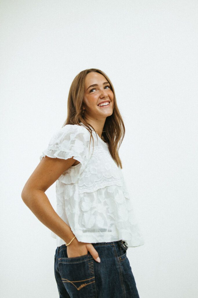 Smiling 18-year-old woman posing in a white blouse and jeans during a studio birthday portrait session.