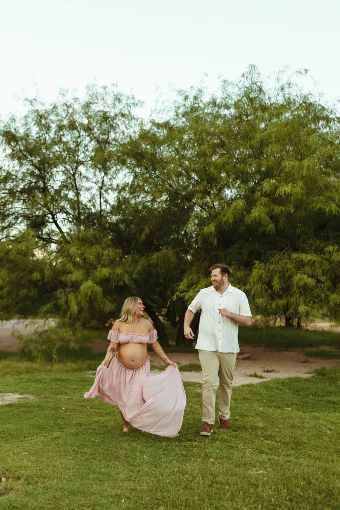 Expecting couple walking and laughing together during their outdoor maternity session at Butcher Jones near Saguaro Lake in Mesa, Arizona