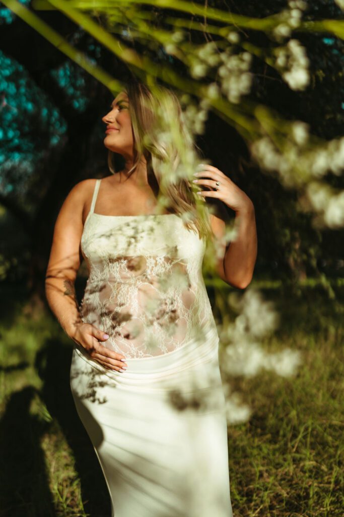 Mother-to-be in a white lace maternity dress surrounded by trees during an Arizona maternity photography session at Butcher Jones