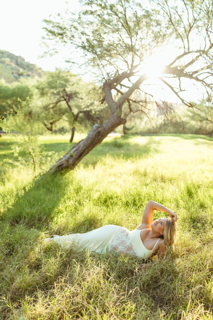 Expecting mother relaxing in sunlit greenery during an outdoor maternity photography session at Butcher Jones in Mesa, Arizona