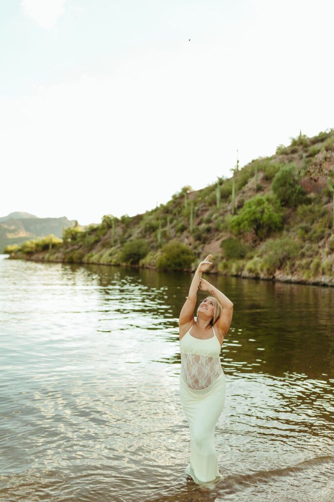 Expecting mother in a white lace maternity dress standing in Saguaro Lake during a Butcher Jones maternity session in Mesa, Arizona