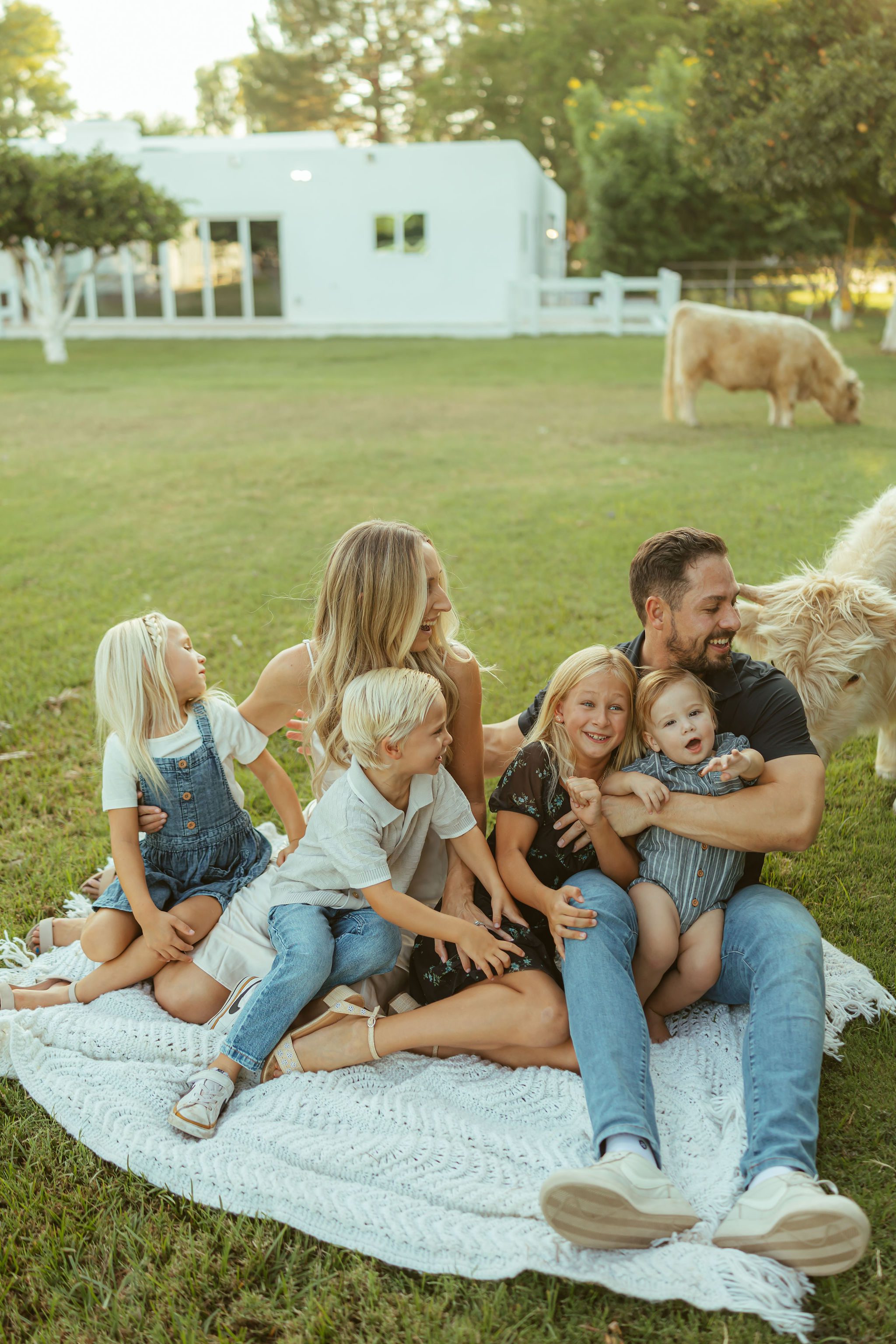 Gilbert family photography session at Bloomstead farm with a large family laughing together on a knit blanket in a green pasture.