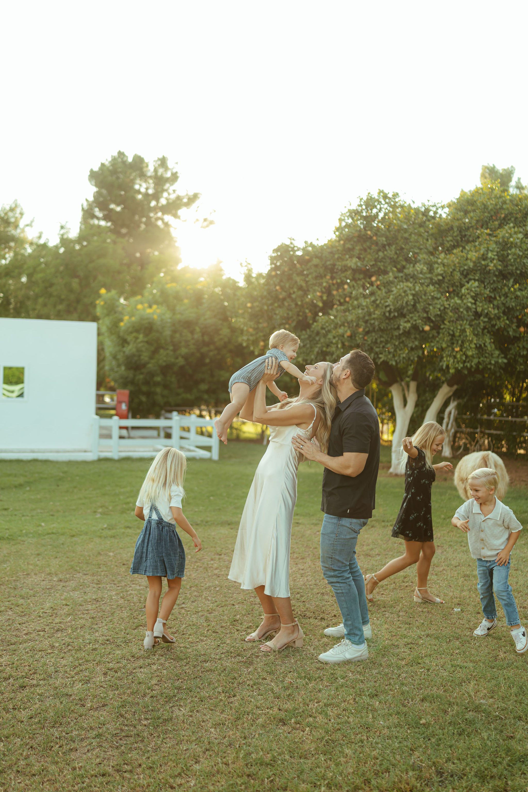 Scottsdale family photographer documenting a fun, effortless lifestyle session as a mother lifts her baby boy in the air while her family plays nearby.