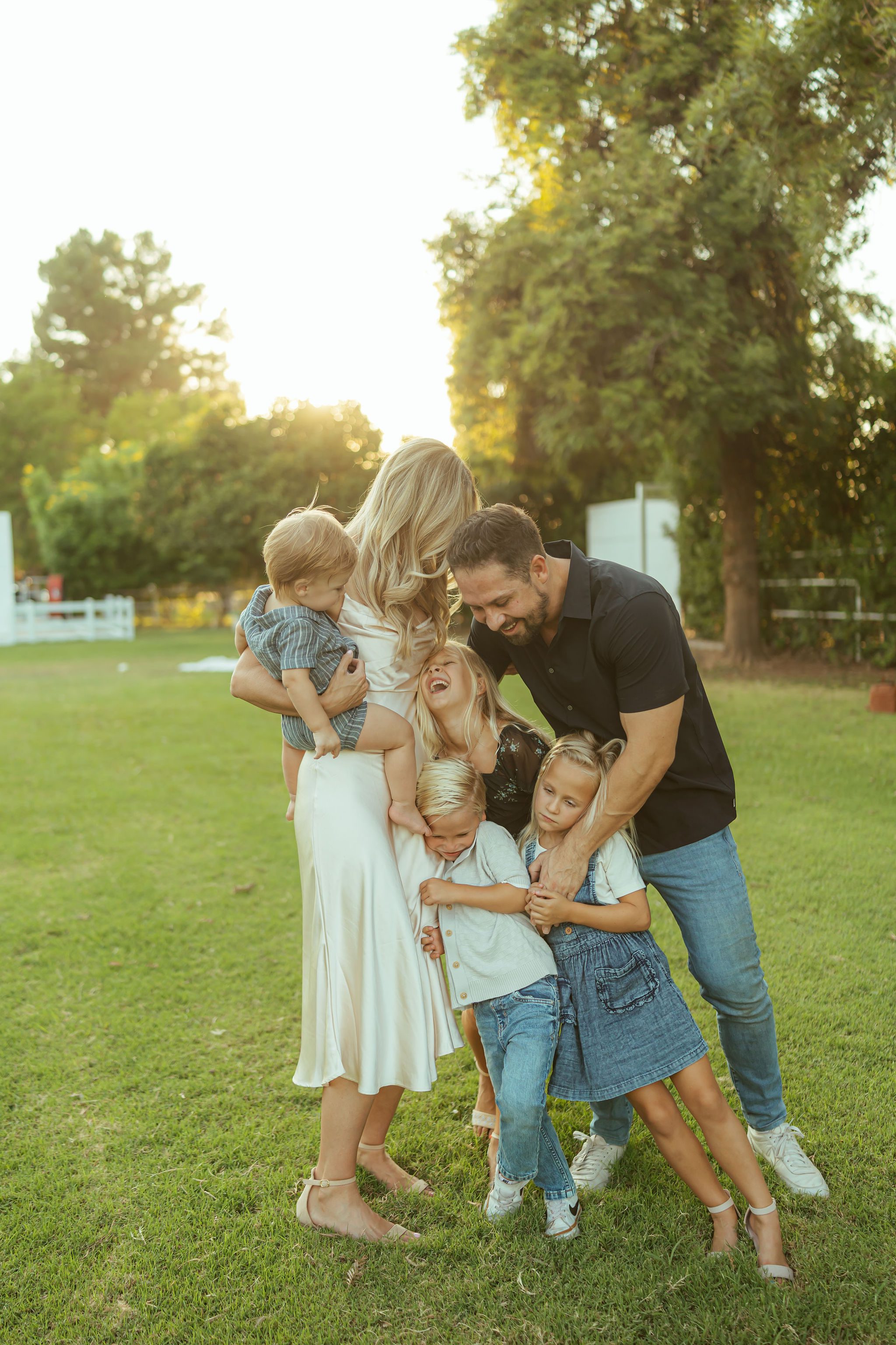 Phoenix family photographer capturing a joyful, tight group hug with a family of seven laughing together in an open grass field at sunset.