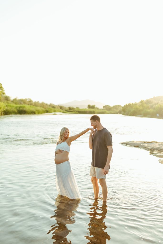 Pregnant woman and her partner standing in the Salt River during their Mesa maternity photography session