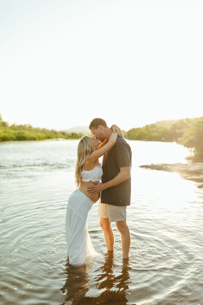 Pregnant couple embracing in the Salt River during a golden-hour maternity session in Mesa
