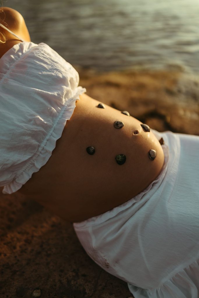 Close-up maternity portrait of pregnant belly with seashells beside the Salt River in Mesa, Arizona
