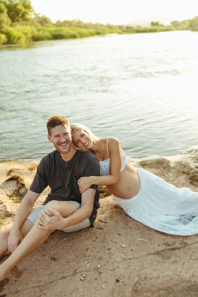 Expecting couple sitting together on the sandy shoreline of the Salt River in Mesa, Arizona