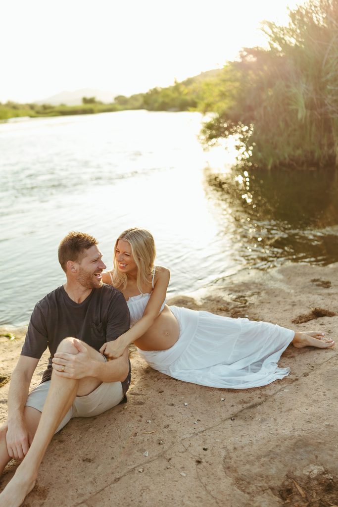 Expecting couple sitting together on the shoreline beside the Salt River in Mesa, Arizona
