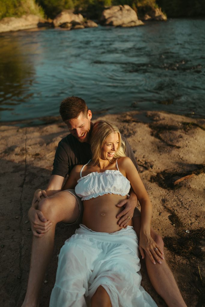 Pregnant couple sitting together beside the Salt River during a golden-hour maternity session in Mesa