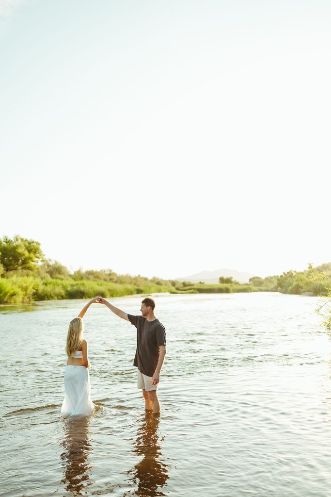 Pregnant couple holding hands and dancing in the Salt River during golden hour in Mesa, Arizona
