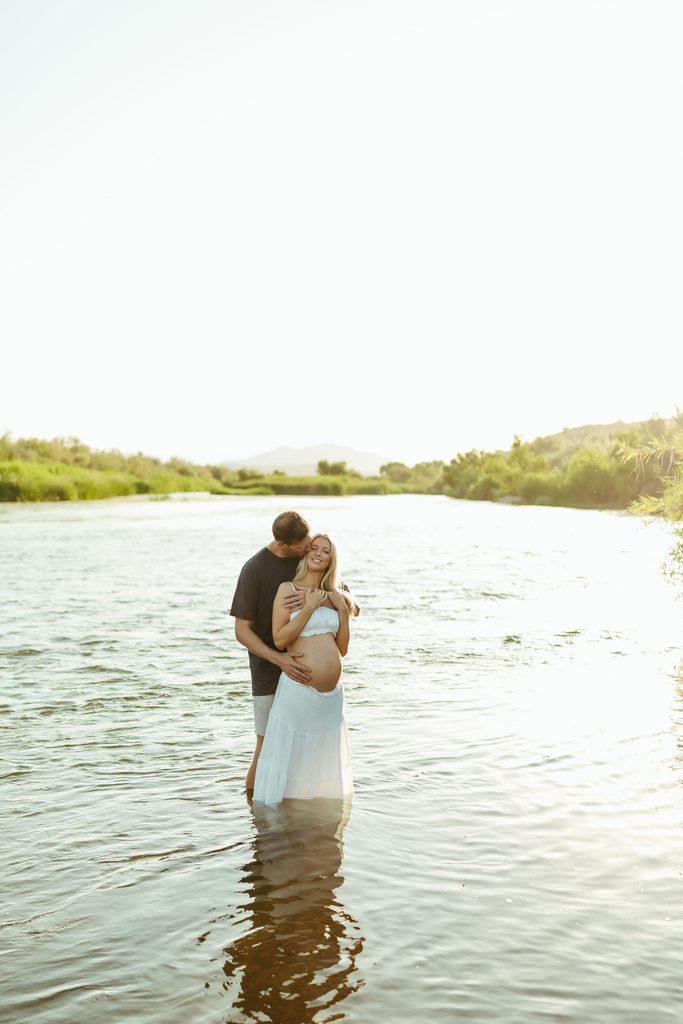 Expecting couple embracing in the Salt River during a romantic Mesa maternity photography session
