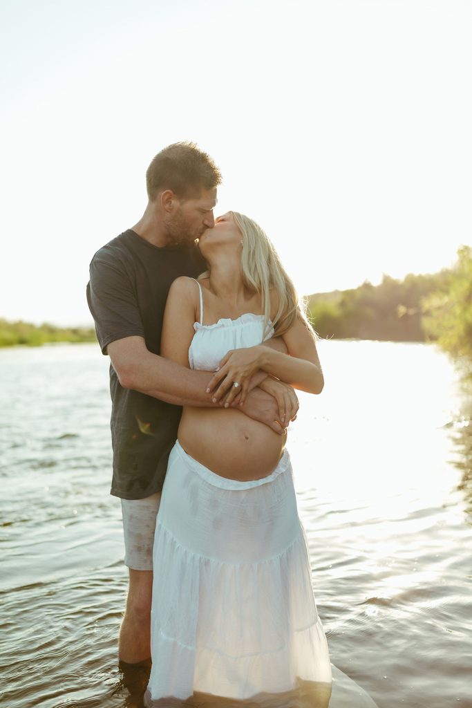 Pregnant couple embracing in the river during a romantic golden-hour maternity photography session