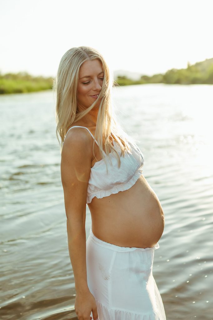 Pregnant woman standing alone in the river during a golden-hour maternity session