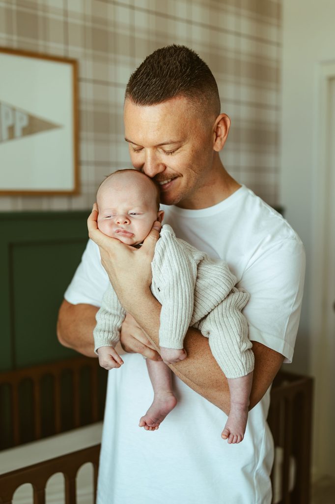 Gilbert newborn photographer photographing a father smiling while holding his newborn baby during an intimate in-home newborn session.