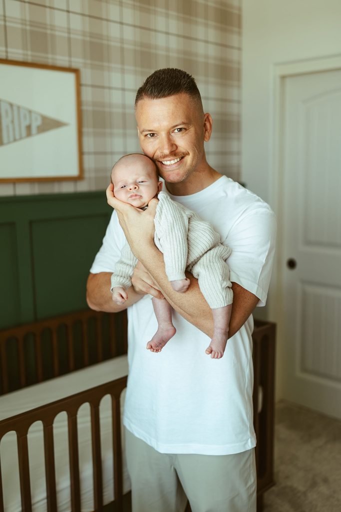 Gilbert newborn photographer capturing a father holding his newborn baby while sitting in the nursery during a lifestyle newborn session.