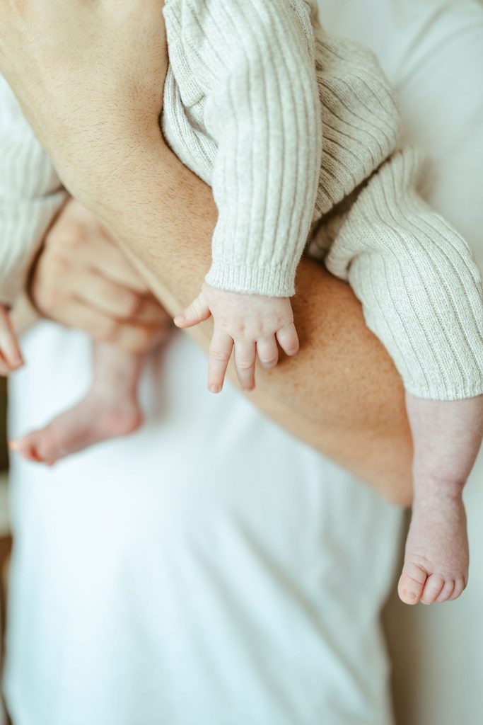 Close-up newborn photography of a baby's tiny hand and feet while being held by a parent during a Gilbert in-home newborn session.