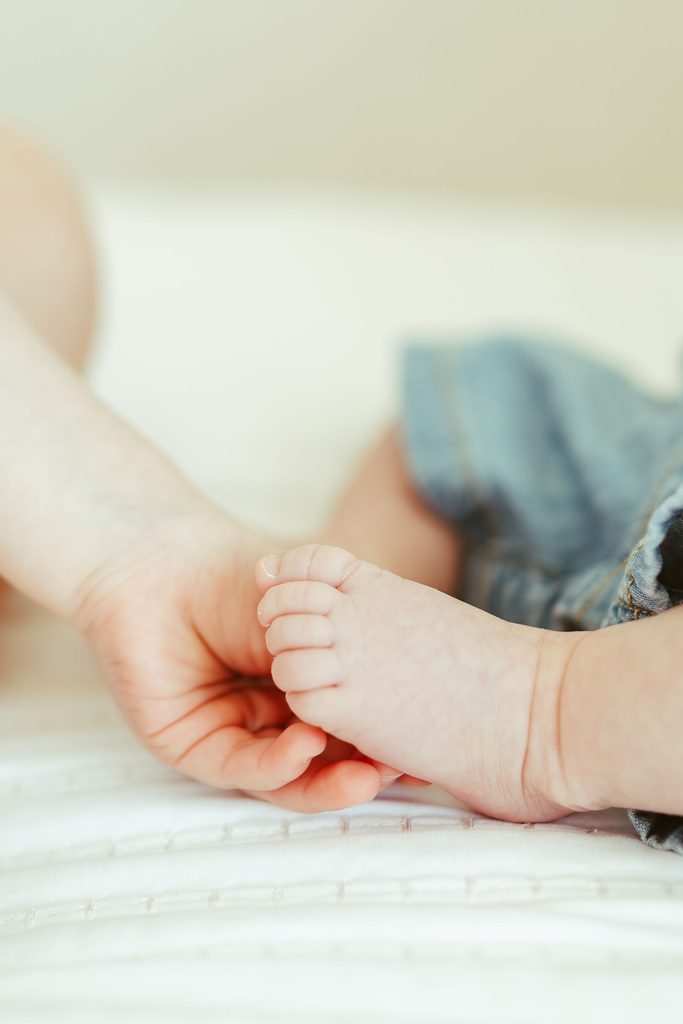 Lifestyle newborn photography in Gilbert capturing a close-up of a newborn baby's tiny feet resting in a parent's hands.