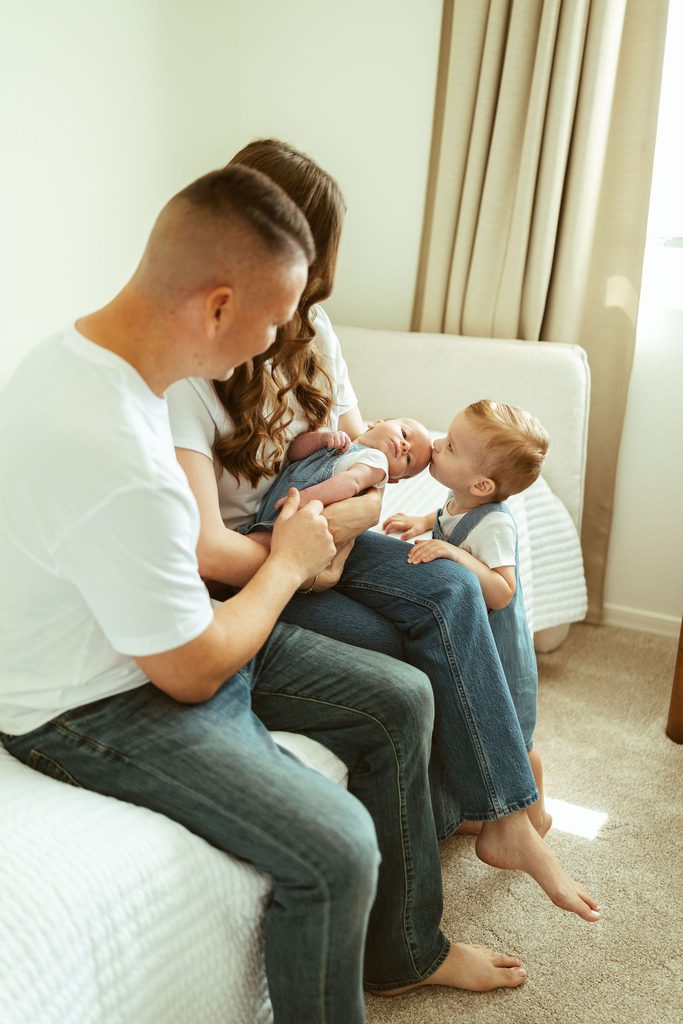 Gilbert newborn photographer capturing a father and mother cuddling their newborn and toddler together on the bed during an in-home family session in Gilbert, Arizona.
