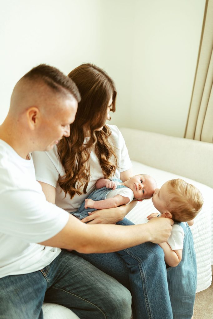 In-home newborn photography in Gilbert, Arizona featuring parents cuddling their newborn and toddler together on the bed