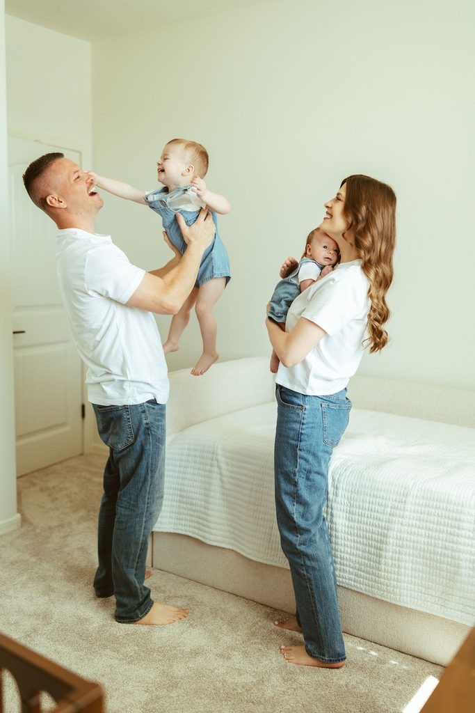 Gilbert family photographer capturing parents lifting their toddler and holding their newborn together during a playful in-home newborn session.