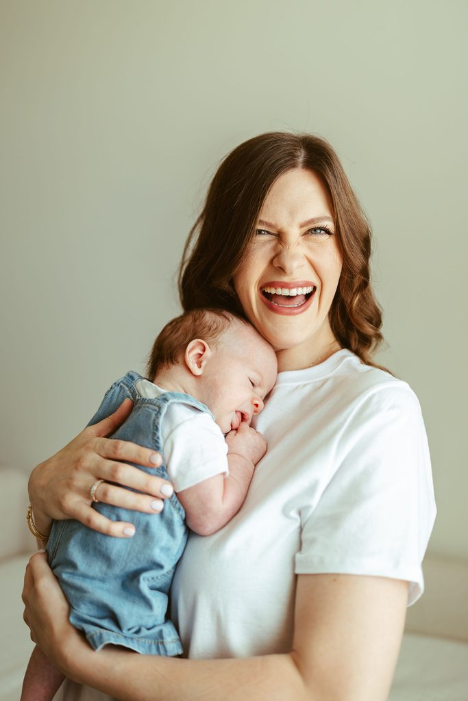 Gilbert newborn photography featuring a smiling mother holding her newborn baby during a relaxed lifestyle session at home.
