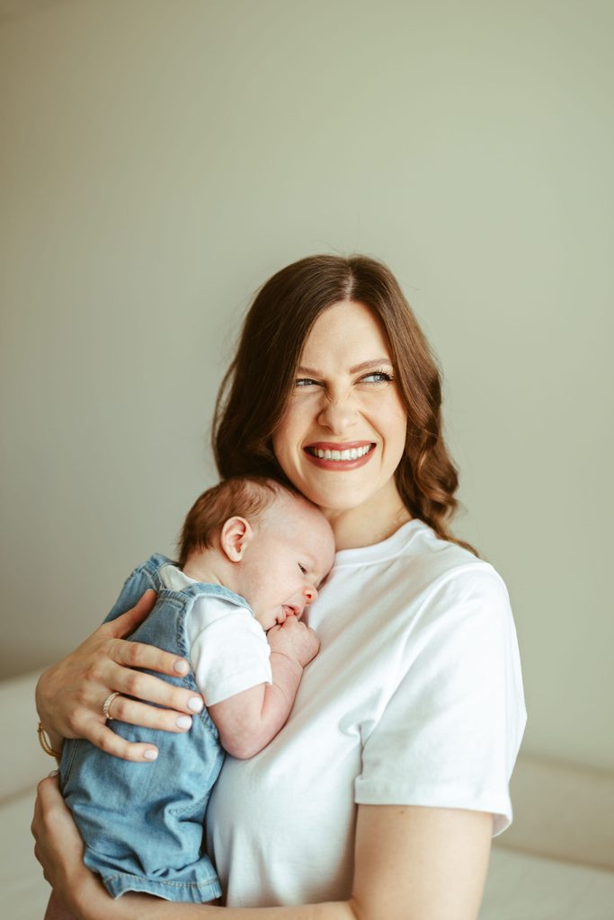 Gilbert newborn photography featuring a smiling mother holding her newborn baby in a bright, cozy nursery.