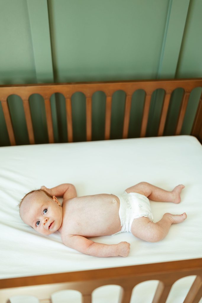 Gilbert newborn photography featuring a newborn baby lying peacefully on a white crib mattress during an in-home lifestyle newborn session.