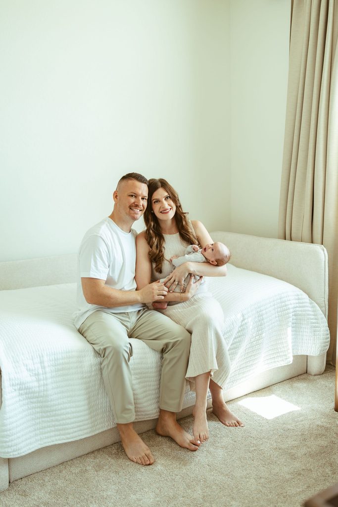 Gilbert family newborn photographer capturing new parents cuddling their newborn baby together on the bed during an in-home session.