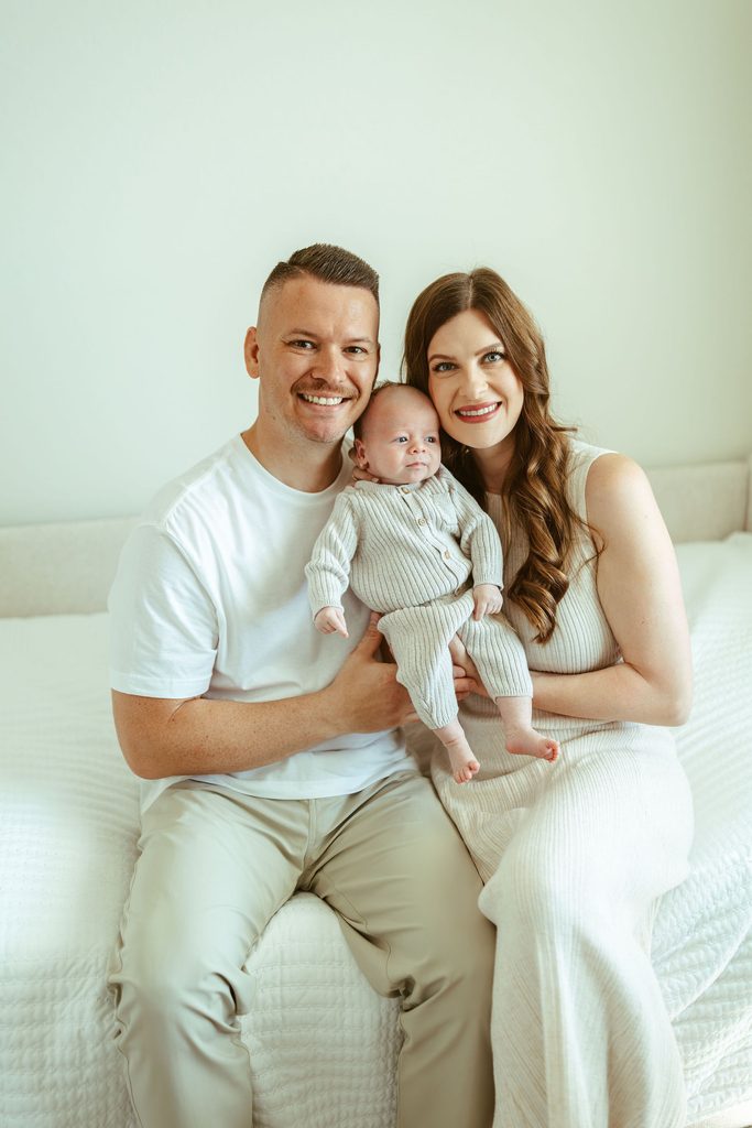 Gilbert newborn photographer capturing new parents smiling while holding their newborn baby together during a beautiful in-home newborn session in Gilbert, Arizona.