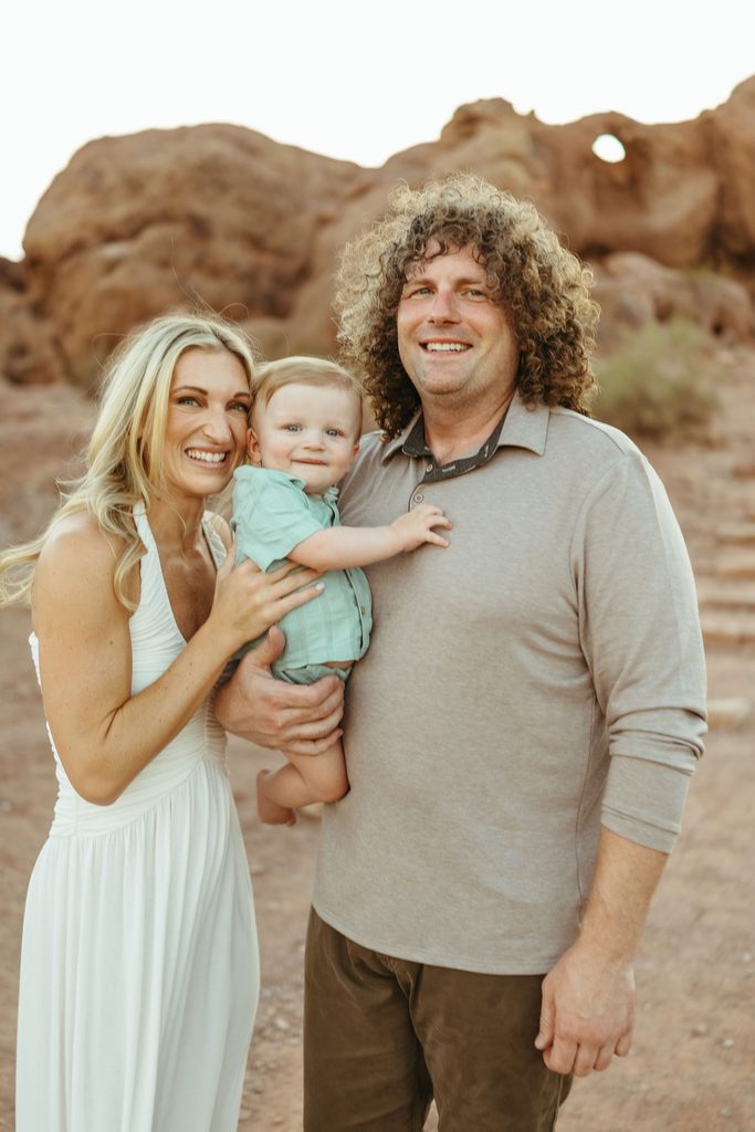 Phoenix family photographer capturing a bright, true-to-color portrait of a family of three standing outside at Papago Park Hole in the Rock.